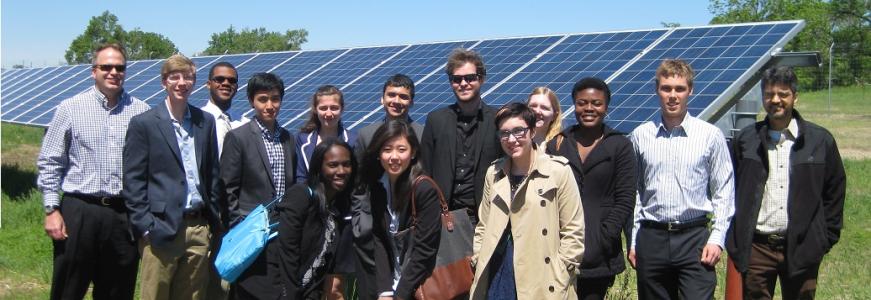 Group of students dressed in business casual standing in front of a solar panel.